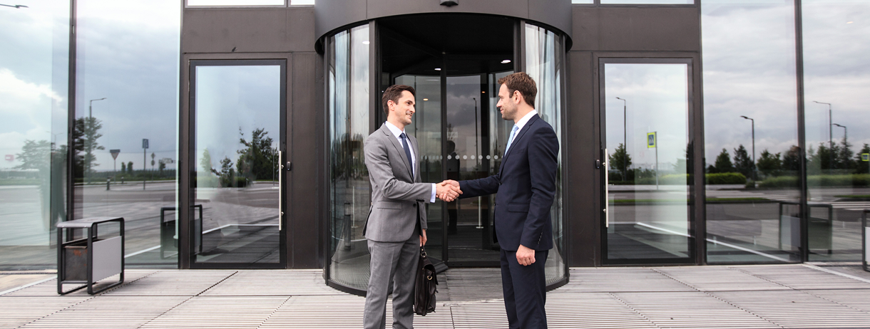Two businessmen shaking hands outside building.